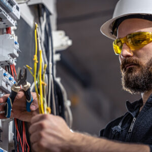 Male electrician at the checkout counter on a blurred background of a switchboard.